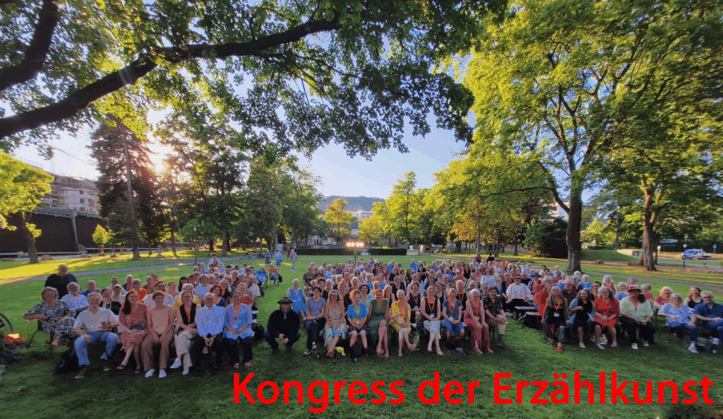 Photo aller Besuchenden beim Kongress 2025 im abendbesonnten Kurpark Bad Münster als Titelbild mit Beschriftung "Kongress der Erzählkunst"
